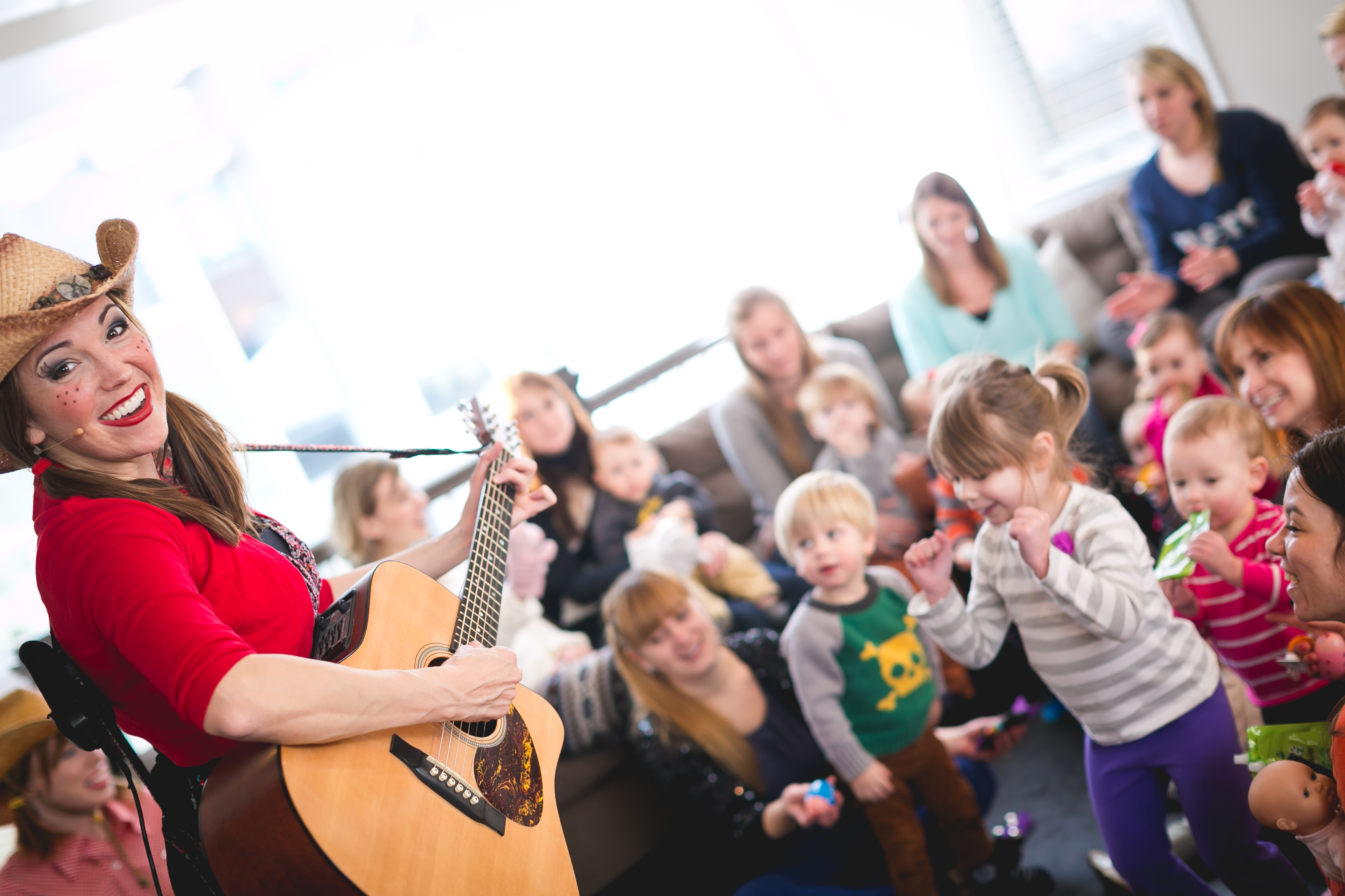 Miss Jamie in a cowboy hat playing guitar while children dance and sing along