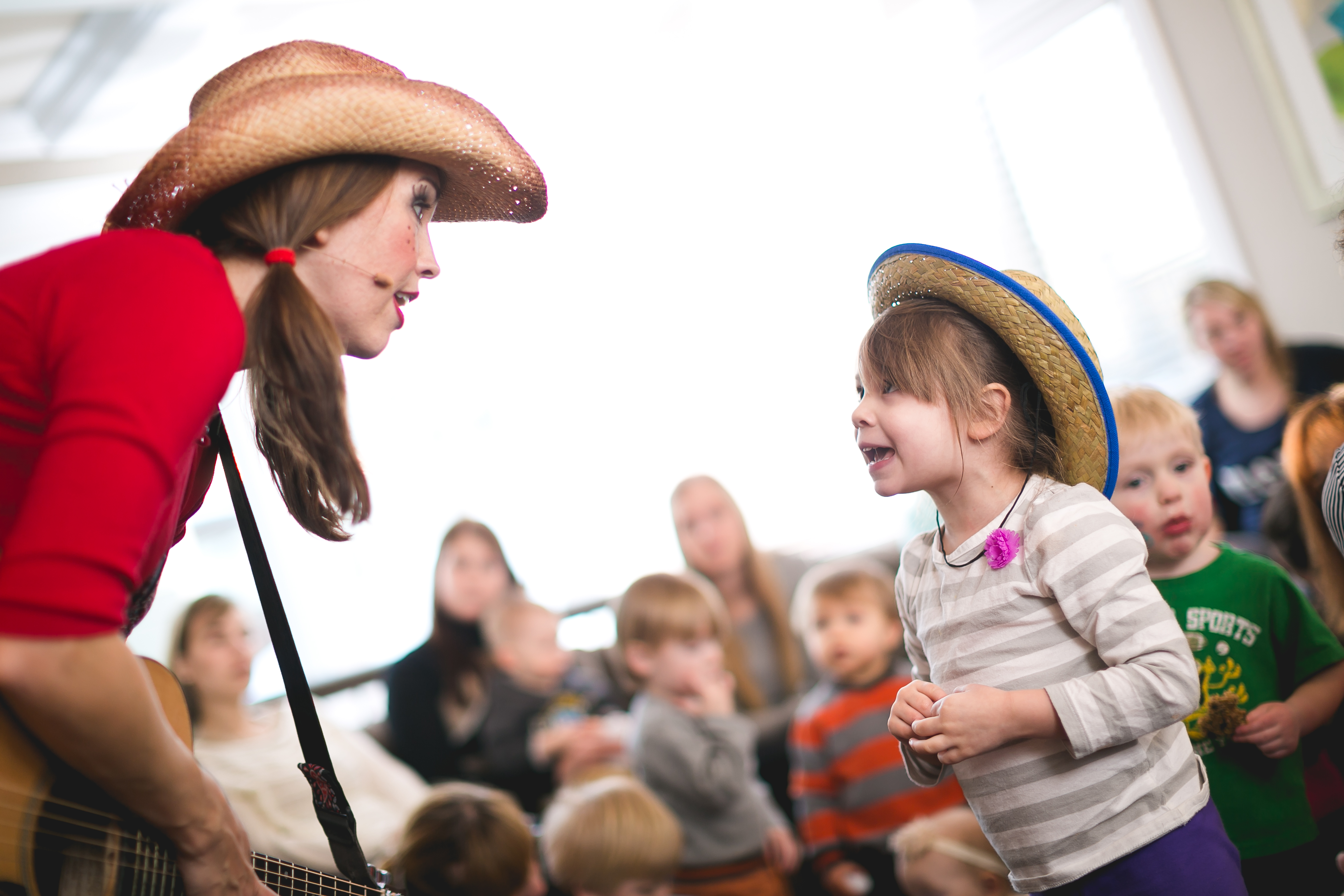 Miss Jamie with guitar singing face to face with a child in a cowboy hat